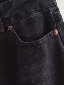 Detail of high-waist black denim pants showing vintage bronze rivets with jeans text