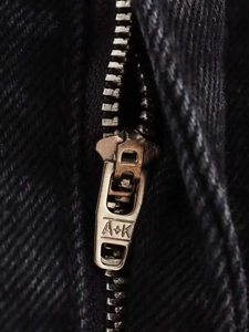 Macro shot of silver metal zipper pull with engraved detail on black denim jeans
