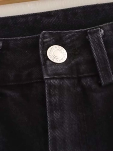 Close-up of silver metal button and textured denim fabric on high waist washed black jeans