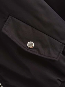Detail of black oversized jacket featuring flap pocket and silver metallic snap button
