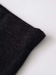 Detail of dark grey knit fabric showing intricate yarn texture and hem finishing