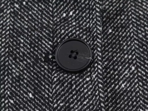 Macro shot of black and white herringbone wool fabric with a matte four-hole button detail