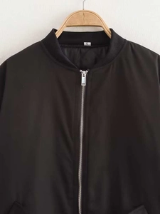 Close-up of black bomber jacket featuring metal zipper and ribbed stand collar detail