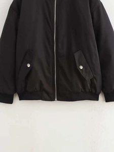 Detail of a black bomber jacket showing the silver zipper and snap button pockets
