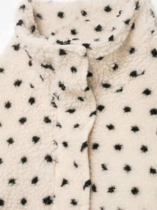 Close-up of cream fleece jacket fabric with black polka dots and metal zipper detail