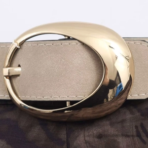 Detail of a beige suede belt featuring a large polished gold oval metal buckle and stitching