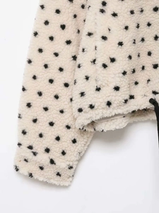 Detail of white fleece jacket featuring black polka dots and an adjustable drawstring hem