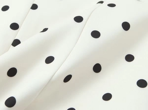 Nahaufnahme von weißem Stoff mit schwarzen Punkten, feiner Textur und weichem Faltenwurf