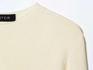 Close-up of cream knit sweater collar showing fine texture and woven brand label