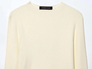 Detailed view of cream knit sweater fabric and neckline with brand label on white surface