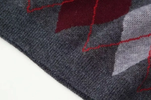 Close-up of thick knitted fabric with grey and burgundy argyle pattern and soft texture