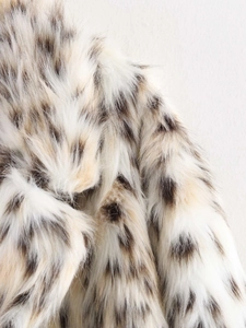 Close-up of fluffy faux fur fabric with leopard animal prints on long winter coat