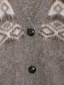 Dettaglio macro del cardigan in maglia tortora soffice con motivi etnici e bottoni marroni