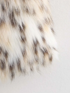 Macro detail of plush faux fur fabric showing soft beige and dark spotted texture