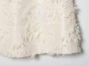 Detail view of cream white fabric featuring textured jacquard and fringe tassel finish