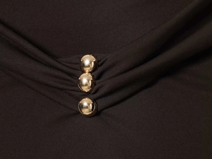 Detail of elegant black pleated dress with vertical gold spherical metal buttons on waist