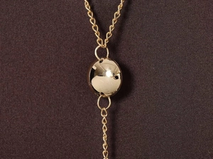 Dettaglio della collana a catena dorata con disco lucido e frangia verticale su abito elegante