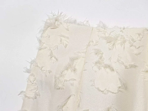 Detailed view of cream-white jacquard fabric with textured 3D fringe and feather accents