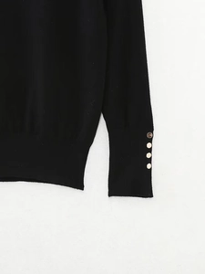 Detail of black knit sleeve cuffs featuring four decorative gold metal buttons on the fabric
