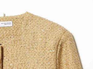 Detailed close-up of golden sequin tweed jacket texture with woven metallic threads