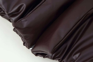 Detailed close-up of dark brown faux leather puffer jacket with quilted padding and zipper