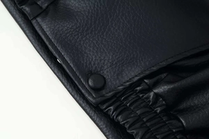 Detail of lychee textured black leather jacket showing matte snap button and elastic hem