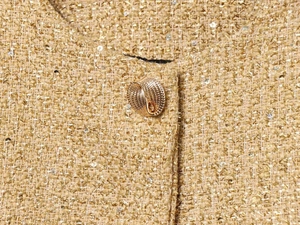 Detail of sandy gold tweed jacket showing shiny sequins and gold spiral button