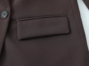Detailed macro view of brown blazer featuring a black button and flap pocket