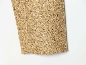 Detailed close-up of gold tweed fabric with sequins and metallic threads for jacket