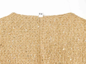 Close-up of golden sequins on tweed fabric with XS size label on the neckline
