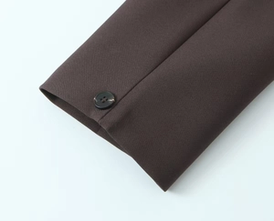 Detail shot of a dark brown blazer sleeve featuring a black four-hole button and woven texture