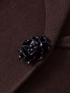 Detail of a black floral jewelry button on a deep brown knit cardigan sweater surface