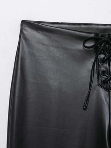 Detailed close-up of black faux leather pants featuring lace-up side design and metal eyelets
