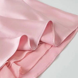 Detail of pink satin fabric showing silky texture and layered wavy hemline of the midi dress