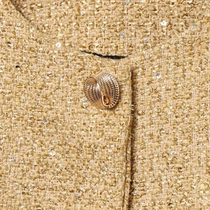 Close-up of golden tweed short jacket with shimmering sequins and embossed metal button