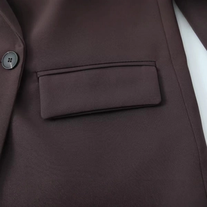 Detail of dark brown blazer featuring a high-quality resin button and flap pocket design