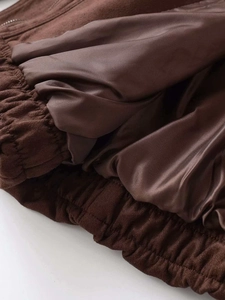 Detail of dark brown suede jacket hem showing smooth satin lining and elastic cuff trim