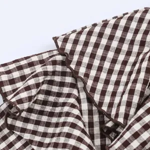 Dettaglio camicia a quadretti con volant marroni e bianchi e cuciture a contrasto