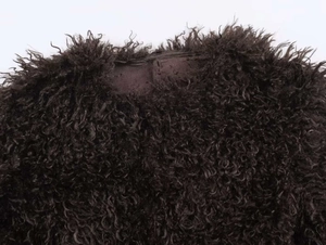 Detail of round neckline on a dark brown curly faux fur coat with thick woolly texture