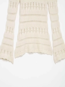 Détail du haut en maille ajourée crème avec bords festonnés et texture du tissu