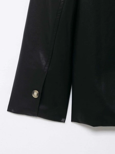 Close-up of black PU leather sleeve with fine stitching and amber texture button detail
