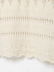 Détail du tricot crème avec découpes géométriques et bordure festonnée élégante en bas
