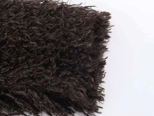 Detailed close-up of dark brown curly faux fur texture with thick and dense wool fibers