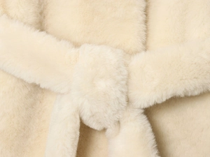 Detailed close-up of cream faux fur jacket texture with a matching waist tie belt