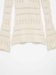 Détail macro du tricot ajouré crème et de l'ourlet ondulé sur un pull en maille cintré
