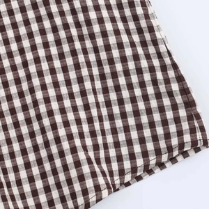 Dettaglio ravvicinato del tessuto in cotone a quadretti marrone e beige della camicia