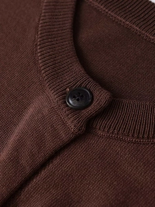 Close-up of dark brown knit cardigan featuring a ribbed neckline and single black button