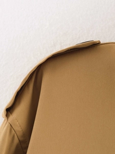 Detailaufnahme der Schulterklappe eines kamelfarbenen Trenchcoats mit Knopf und Köpergewebe