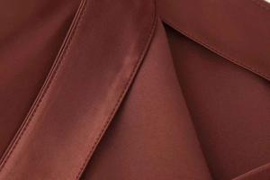 Macro shot of satin fabric showing fine stitching and luxury texture on wine red skirt