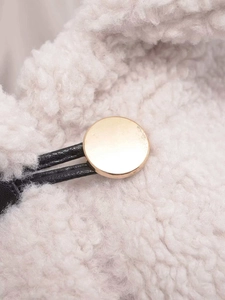 Detailed close-up of golden metal toggle and plush cream faux shearling coat fabric